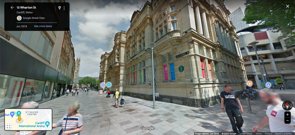 A screenshot of Google Maps Street View, located at 13 Wharton St in Cardiff, Wales. It's in the city centre, with people walking around a mix of historic and modern buildings.